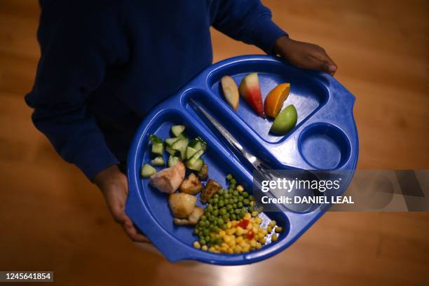 Child carries a tray with food during lunch-break at St Mary's RC Primary School, in Battersea, south London, on November 29, 2022. - With UK...