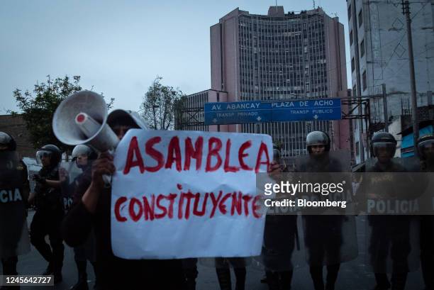 Demonstrator holds a sign as riot police officers stand guard during protests on Avenida de Pierola in Lima, Peru, on Thursday, Dec. 15, 2022. Peru...