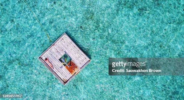 aerial view of a woman sunbathing at the edge of a wooden raft floating above the sea, beach holiday concept - floating moored platform stock pictures, royalty-free photos & images