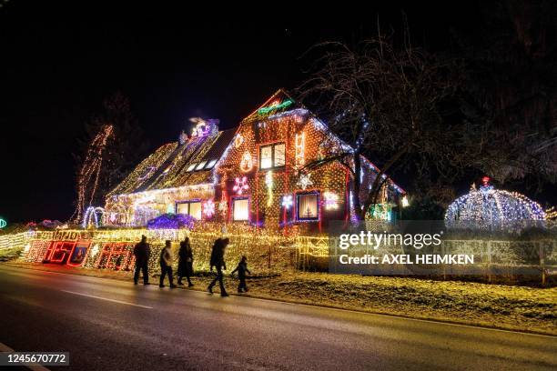 Strollers walk past a house illuminated with Christmas outdoor decoration in Buecken, northern Germany on December 16, 2022.