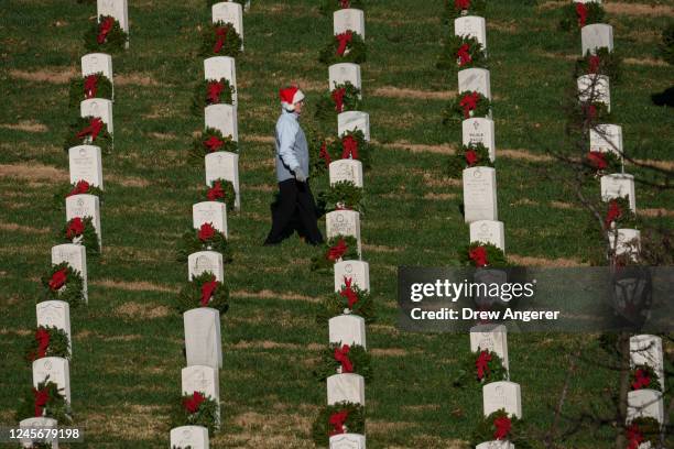 Volunteer wearing a Santa hat places wreaths on headstones at Arlington National Cemetery on December 17, 2022 in Arlington, Virginia. Thousands of...