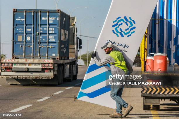 Worker walks with a sign bearing the name and logo of the "Baghdad Conference for Cooperation and Partnership", to be installed along a road amidst...