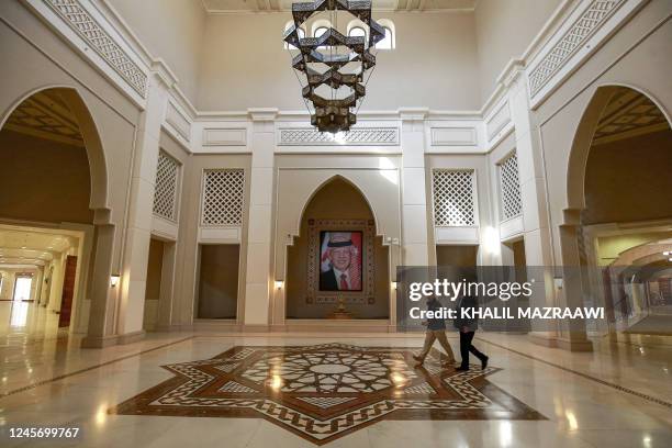 Men walk near a framed picture depicting Jordan's reigning King Abdullah II as they cross the main hall at the King Hussein Bin Talal Convention...