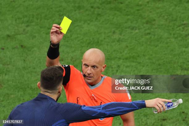 Polish referee Szymon Marciniak shows a yellow card to France's forward Olivier Giroud on the bench during the Qatar 2022 World Cup final football...