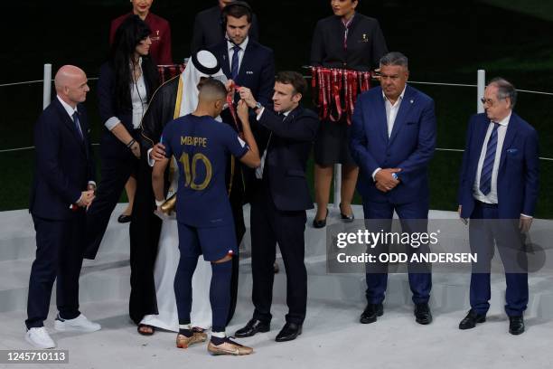 France's forward Kylian Mbappe receives the silver medal by Qatar's Sheikh Tamim bin Hamad al-Thani and French President Emmanuel Macron on the...