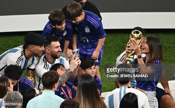 Argentina's forward Lionel Messi takes smartphone pictures of his wife Antonela Roccuzzo holding the World Cup Trophy at the end of the Qatar 2022...