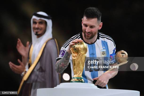 Argentina's forward Lionel Messi touches the trophy as he holds the Golden Ball award during the Qatar 2022 World Cup trophy ceremony after the...