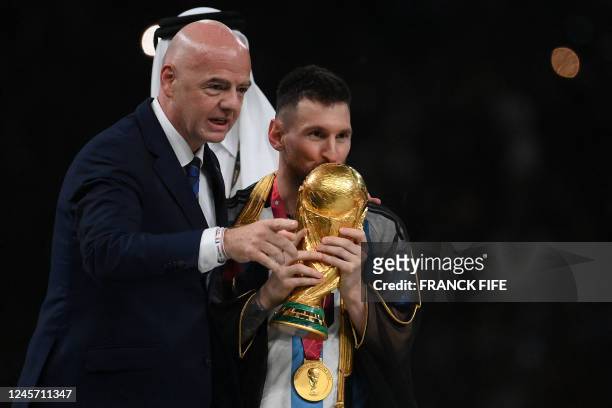 Argentina's forward Lionel Messi kisses the World Cup trophy after receiving it from FIFA President Gianni Infantino next to Qatar's Emir Sheikh...