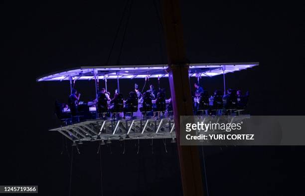 People sit at tables on a platform of the first hanging restaurant to be opened to the public in Venezuela in the Altamira neighborhood of Caracas on...