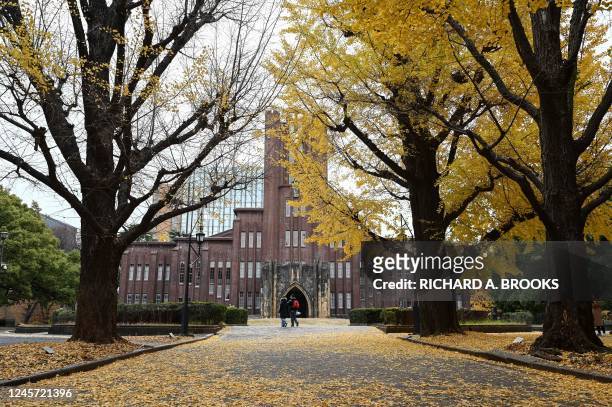 This photo taken on December 17, 2022 shows people walking past autumn leaves which have fallen in front of Yasuda Auditorium, build in 1925 and at...