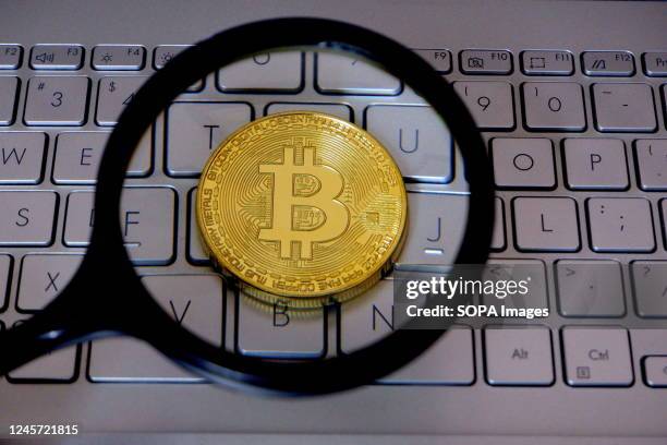 In this photo illustration, a cryptocurrency bitcoin is seen through a magnifying glass on a laptop keyboard.