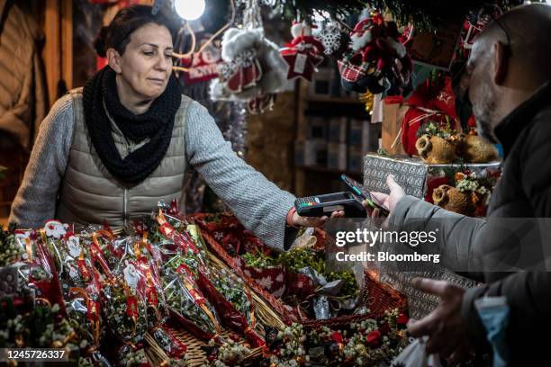 Customer uses a contactless payment terminal to pay with a smartphone for a purchase on a stall at the Fira de Santa Llucia Christmas market in...