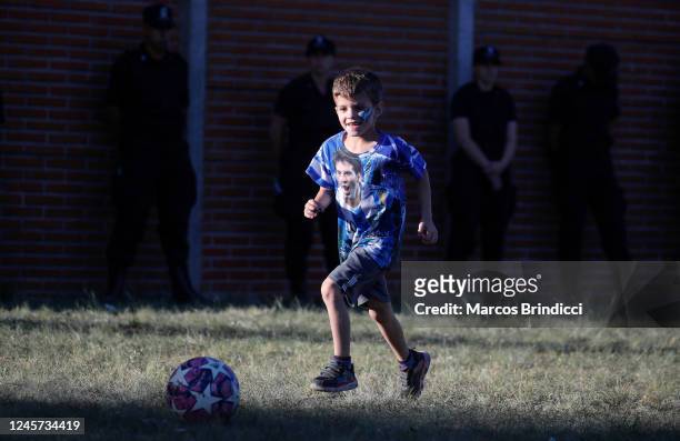 Boy wearing a jersey with a portrait of Lionel Messi plays football as waiting for the arrival of the Argentina men's national football team after...