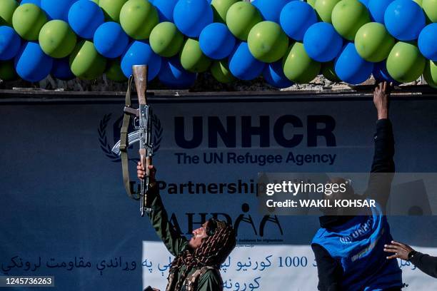 In this photo taken on December 15 a member of Taliban security adjust balloons with his gun during a handover ceremony of newly built houses...