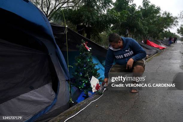 Venezuelan migrant Saul Molina turns on the lights of a Christmas tree that he got for his children at a makeshift camp near the Gateway...