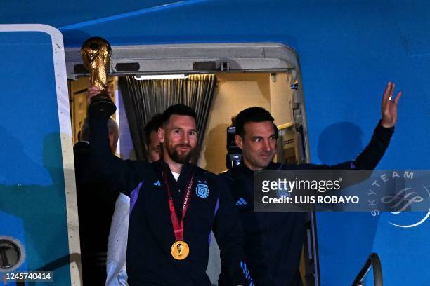 Argentina's captain and forward Lionel Messi holds the FIFA World Cup Trophy alongside Argentina's coach Lionel Scaloni as they step off a plane upon...