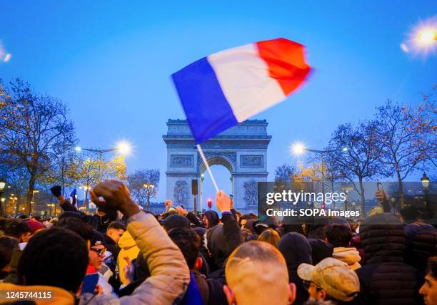 Soccer fan waves a French flag with the backdrop of Arc de Triomphe, during 2022 World Cup final. French football fans gather on the Champs Elysees,...