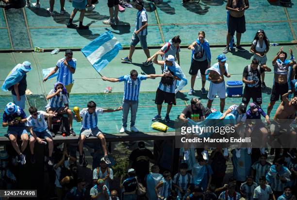 Fans of Argentina stand on the rooftop of a bus stop as they celebrate with flags during a victory parade of the Argentina men's national football...