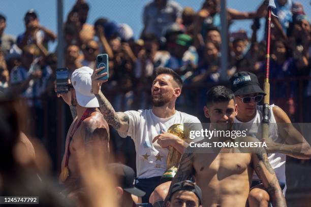 Argentine football star Lionel Messi takes pictures with his phone while celebrating on board a bus with a sign reading "World Champions" with...