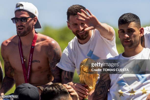 Argentine players Rodrigo De Paul , Lionel Messi and Cristian Romero celebrate on board a bus with a sign reading "World Champions" with supporters...