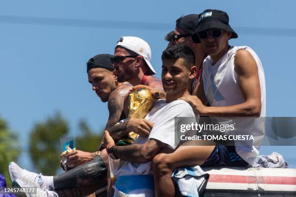 Argentina's Cristian Romero holds the FIFA World Cup Trophy next to Rodrigo De Paul and Nahuel Molina as they parade on board a bus after winning the...