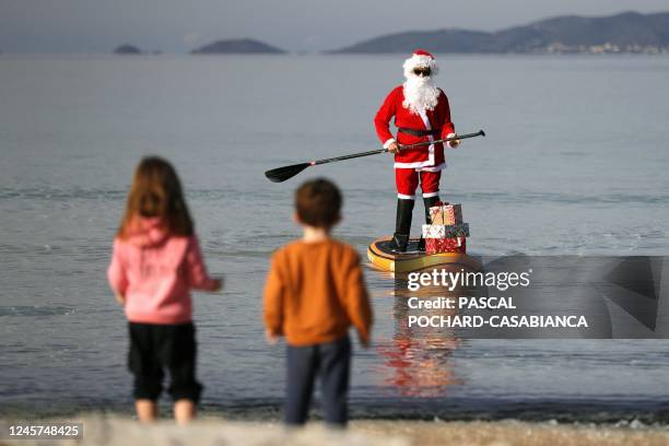 Children wait for a woman dressed as Santa Claus steering a paddleboard close to the Mare e Sol beach in Pietrosella on December 20, 2022 on the...
