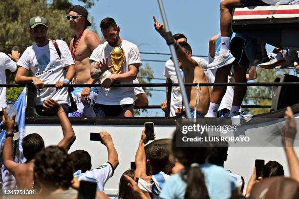 Argentina's Lionel Messi waves at fans holding the FIFA World Cup Trophy as the team parades on board a bus after winning the Qatar 2022 World Cup...