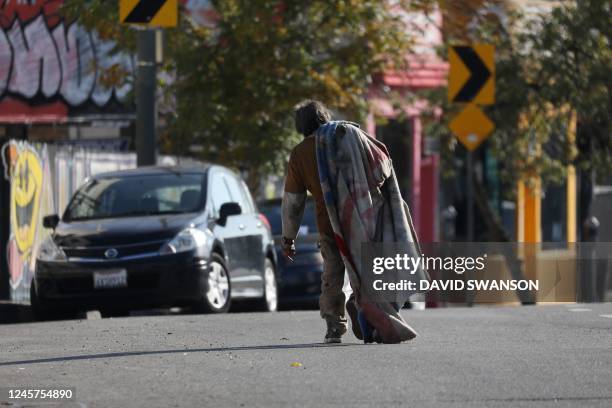 An unhoused person carries their blanket along Sunset Boulevard in Los Angeles, California, December 19, 2022. - A state of emergency over spiraling...