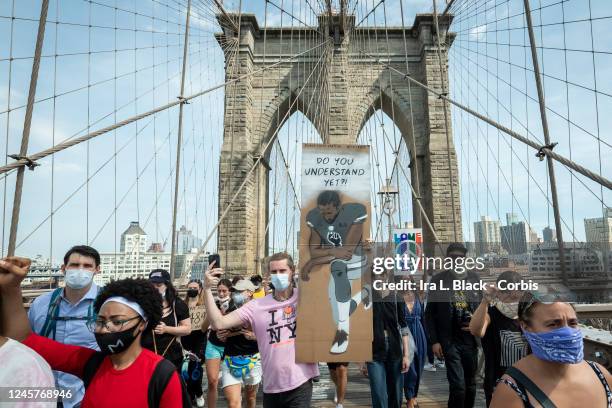 Caucasian protester wearing a mask holds a sign that says,"Do You Understand Yet?" with a picture of Colin Kaepernick, former quarterback for the San...