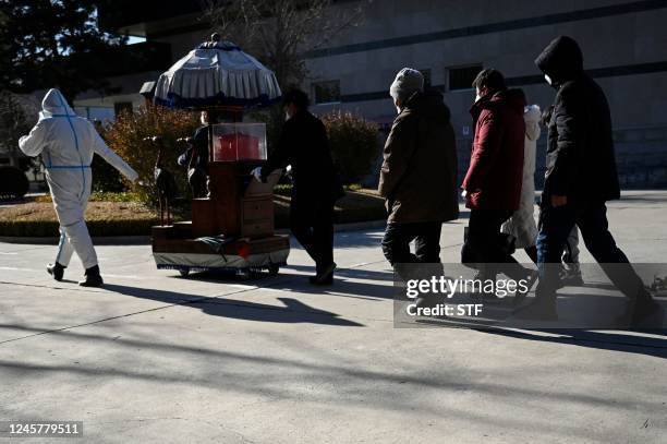 Family members follow an urn containing the ashes of a loved one at a crematorium in Beijing on December 22, 2022. - Hospitals are struggling,...