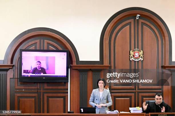 Officials look on as Georgia's ex-President Mikheil Saakashvili appears on a screen via a video link from a clinic during a court hearing in Tbilisi...