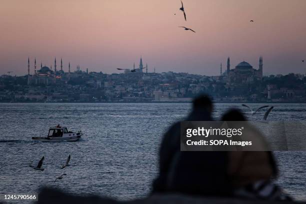As the sun sets on Kadikoy beach in Istanbul, a couple seen sitting on the cliffs and flying seagulls passing by.