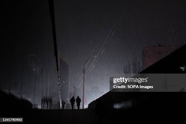 Lonely passers-by are seen emerging from an underpass at night during a snowfall during a blackout in Kyiv. The streets of Ukraines capital are...