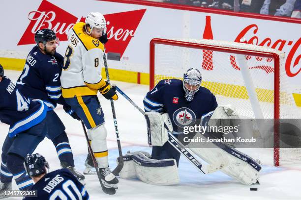 Goaltender Connor Hellebuyck of the Winnipeg Jets makes a save as Cody Glass of the Nashville Predators looks on during third period action at Canada...