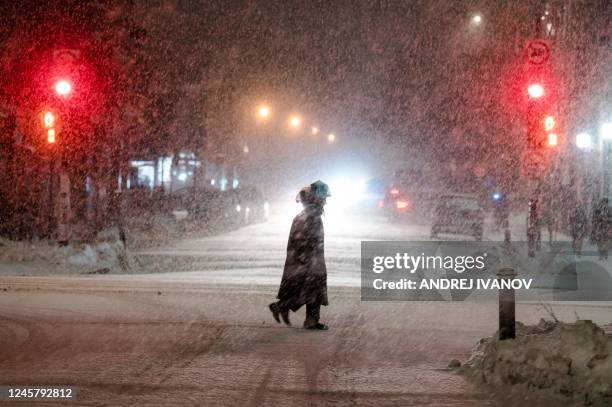 People cross a street in the Mile End, a borough in Montreal, Quebec, Canada, as the snow comes down on December 22, 2022. - A "once-in-a-generation"...