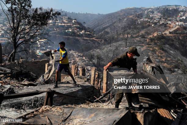 Men remove debris from houses destroyed by a forest fire in the hills of Vina del Mar, in the Valparaiso region, Chile, on December 23, 2022. - At...