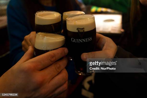 Young people toasting inside a pub with half pints of Guinness black beer, the most popular in Dublin .