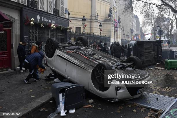 People pass by cars which have been turned over during clashes following a demonstration of members of the Kurdish community, a day after a gunman...