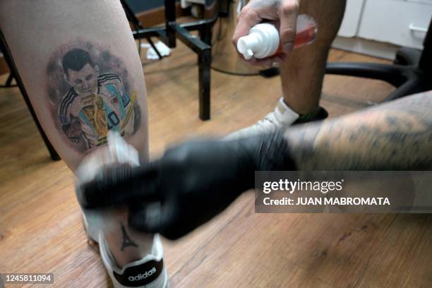 Tattooist Dario Vivas protects the tattoo of Argentina's Lionel Messi kissing the FIFA World Cup trophy on the leg of Nicolas Rechanik at Face Tattoo...