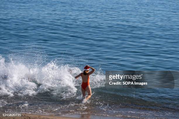 Woman wearing a Santa Claus hat enters the water on the beach to take a bath. As a Christmas tradition, and taking advantage of the high...