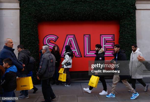 Shoppers walk past sale promotion signage at the Selfridges Ltd. Department store on Oxford Street during traditional Boxing Day holiday sales, in...