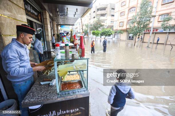 Palestinian man makes meals at his restaurant near a flooded road after heavy rains due to a winter storm hitting the Gaza strip at the Al-Shati...