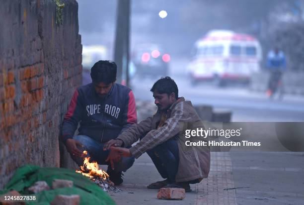 People huddle around a bonfire to warm themselves amid fog and cold weather, at Geeta Colony on December 26, 2022 in New Delhi, India. Dense fog...