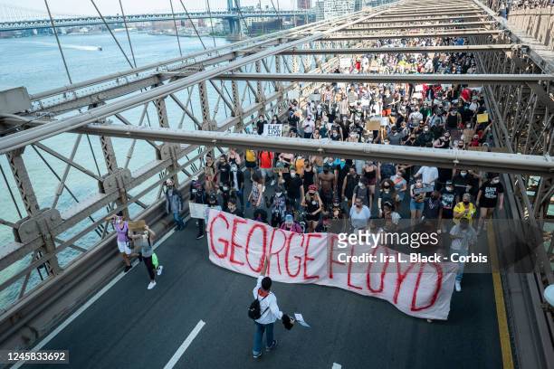 Protesters march with a banner that says, "Justice for George Floyd" as thousands of protesters walk across the Brooklyn Bridge with the Manhattan...