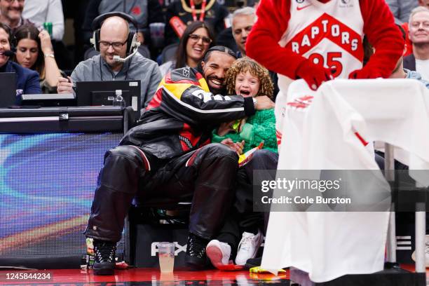 Rapper Drake embraces his son Adonis as the Raptor mascot brings over candy for him during the first half of the NBA game between the Toronto Raptors...