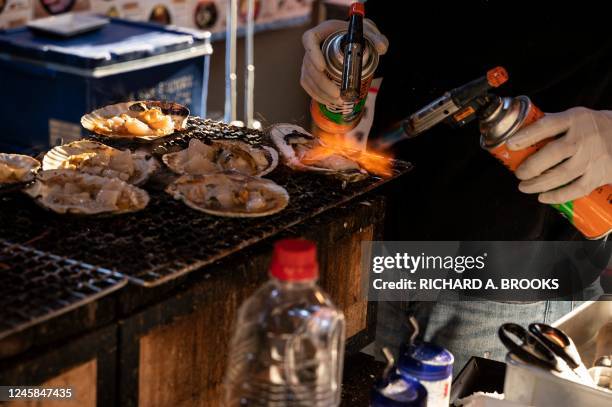 Vendor uses blowtorches on fresh seafood in the Tsukiji "outer fish market" area in Tokyo on December 28 as foreign tourists and locals visit ahead...