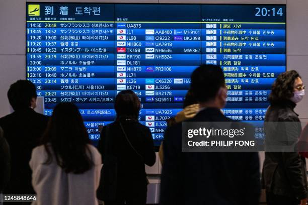 People wait in front a board showing international flight arrivals at Tokyo's Haneda international airport on December 28, 2022. - Hong Kong...