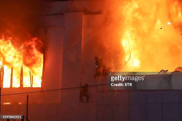 Fire burns around people on a ledge on the side of the Grand Diamond City hotel-casino in Poipet on December 29, 2022. - As many as 10 people have...