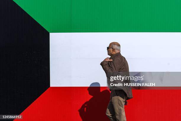 Man walks along the pavement next to a large banner depicting the flag of Kuwait as part of preparations ahead of the 25th Arabian Gulf Cup football...