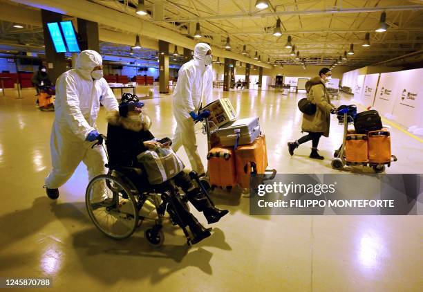 Workers wearing protective masks and suits help Chinese travellers leaving the arrival hall of RomeFiumicino International Airport, near Rome, on...